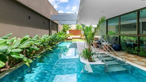 A modern indoor pool with clear blue water, surrounded by lush greenery and a glass wall. - Flat Boutique em Casa Forte CFP105 (Recife)
