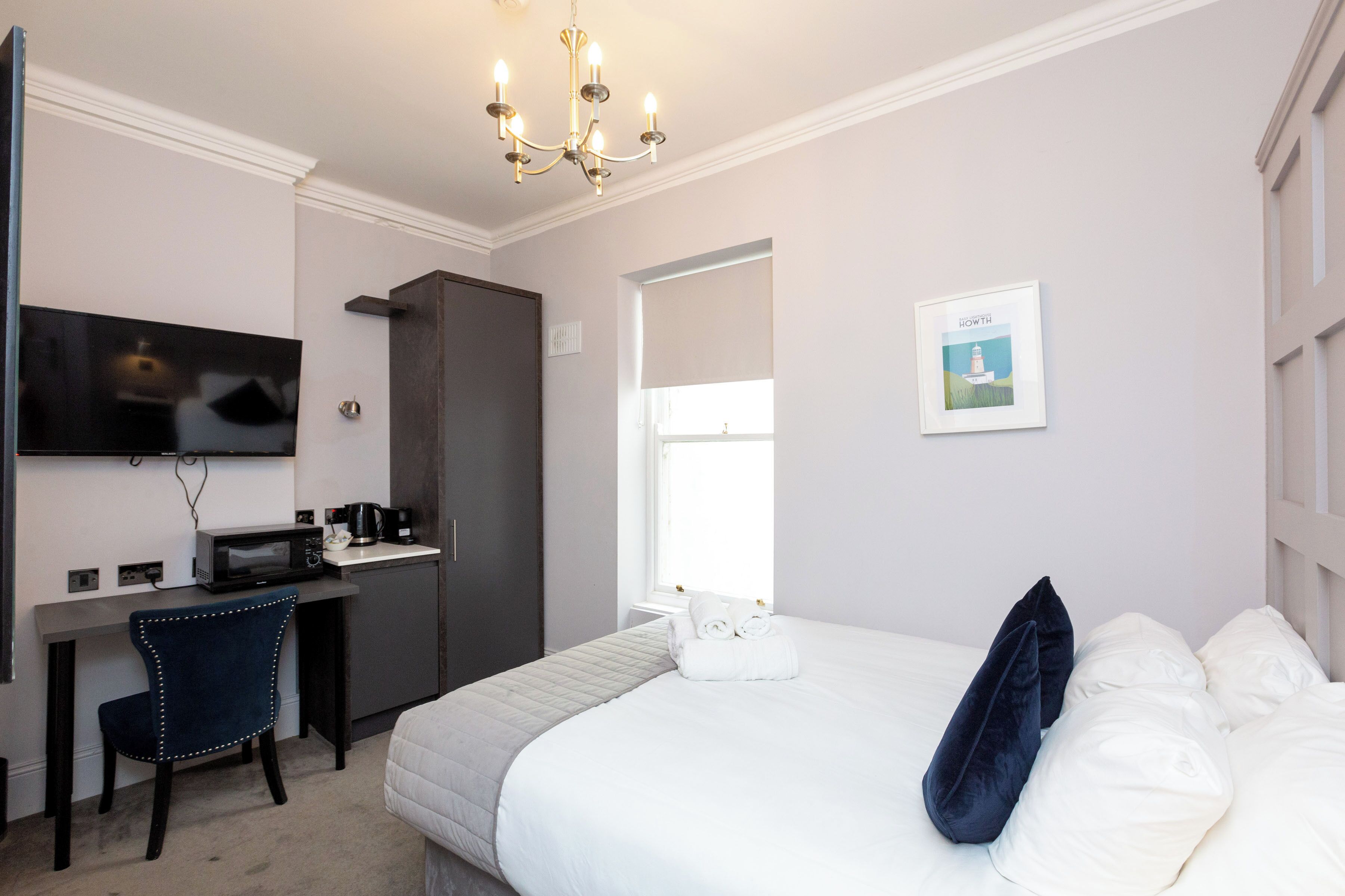 Quarto de hotel com cama, escrivaninha com micro-ondas, cadeira, televisão e janela com vista para um farol.
