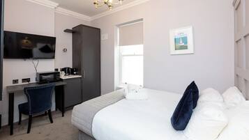 Quarto de hotel com cama, escrivaninha com micro-ondas, cadeira, televisão e janela com vista para um farol.