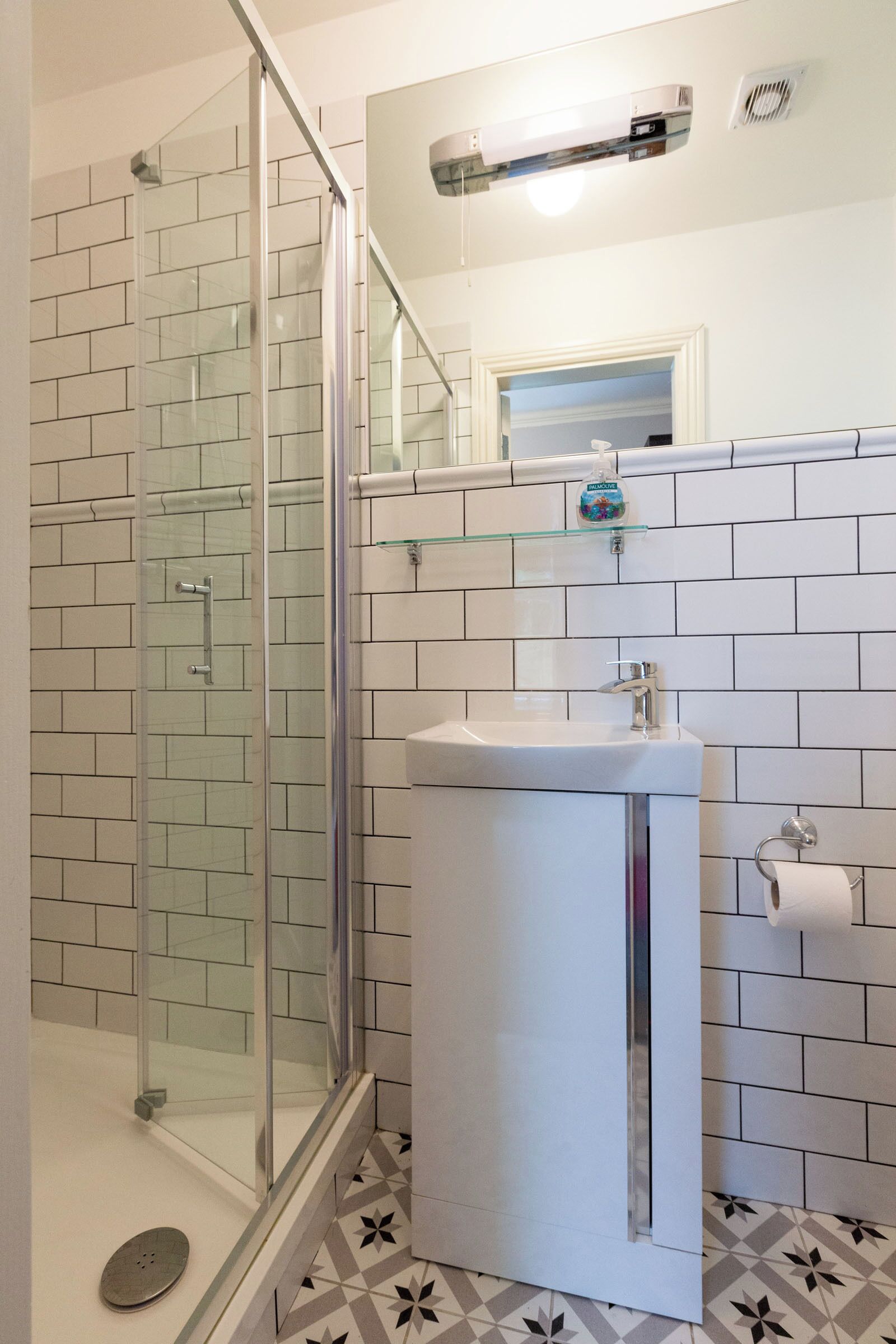 Un baño con cabina de ducha de vidrio, un lavamanos blanco y suelo de baldosas.