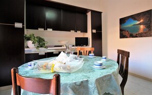 A dining area with a table set for two, a television in the background, and a painting on the wall. - FOUR-ROOM APARTMENT ON THE 1ST FLOOR (Santa Teresa Gallura)