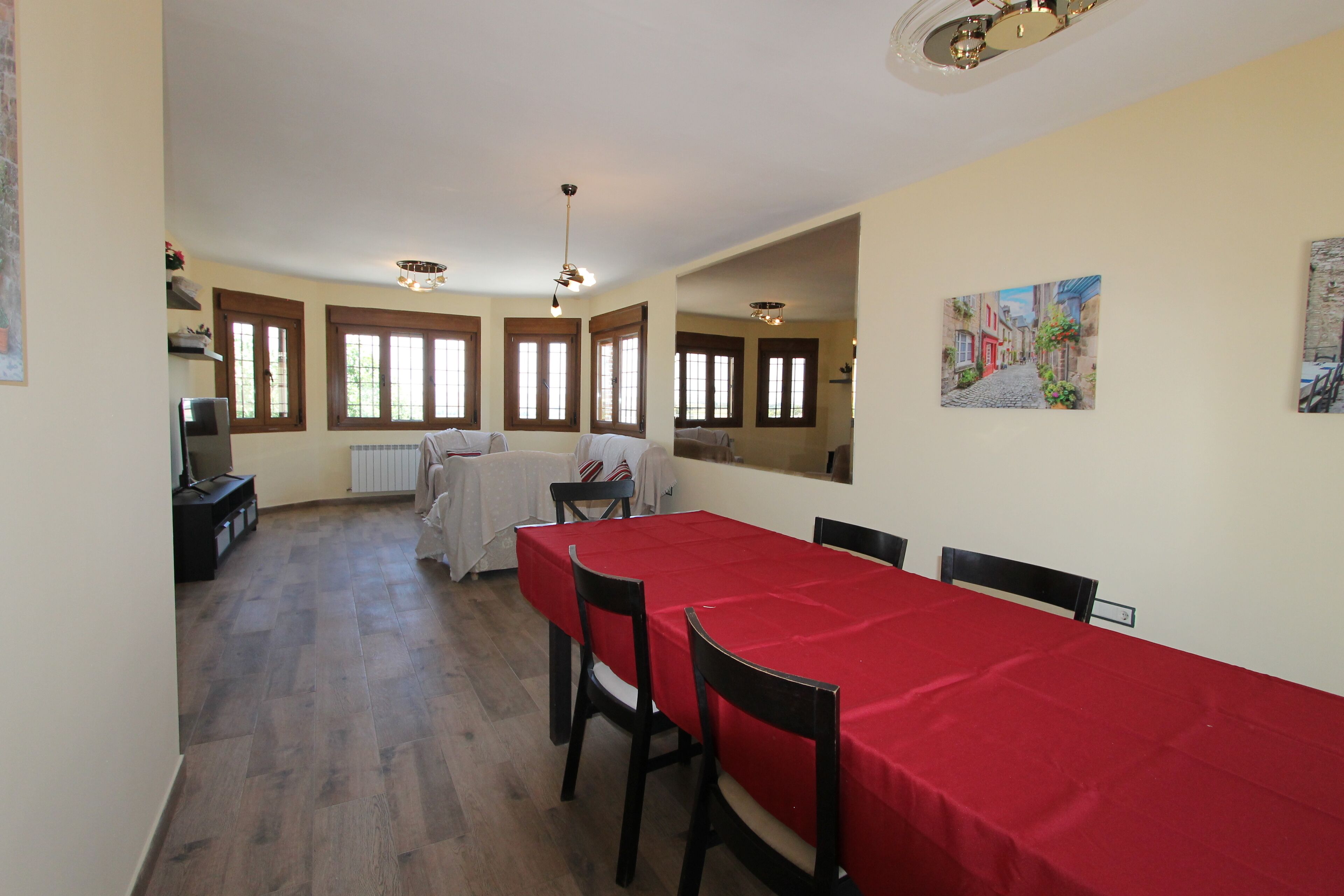 A dining area with a red tablecloth, wooden chairs, and a view of a street through the window.