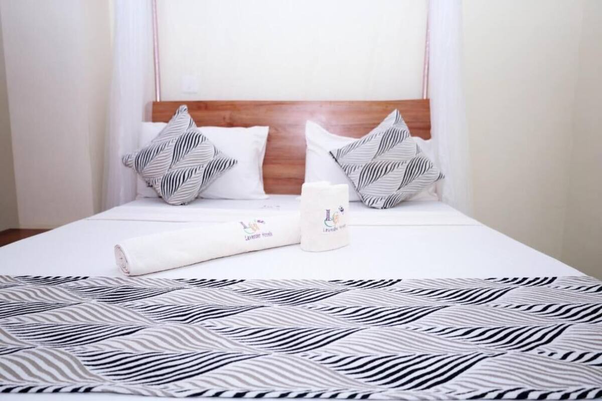 A neatly made bed with a patterned bedspread, two pillows with a zebra print, and a rolled towel with a logo.