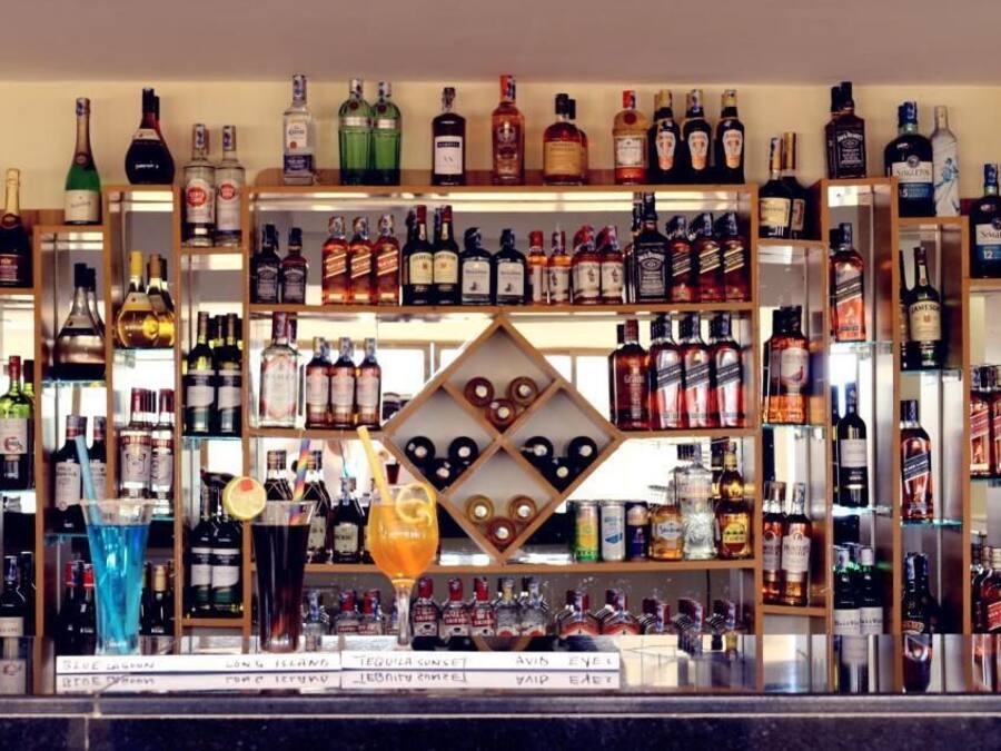 Zona de bar con estantes llenos de botellas de licores y una exhibición central de vasos.