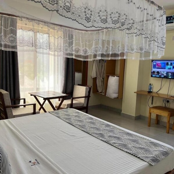 A hotel room with a bed, a small table, a chair, a TV, and a window with curtains.
