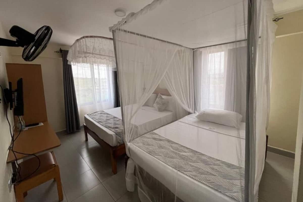 A room with two single beds, a desk, and a ceiling fan.