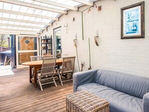 Eine Holzterrasse mit Tisch und Stühlen, einem grauen Sofa und einem Korbwannenstuhl.