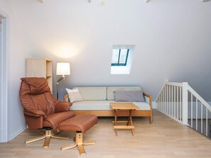 A room with a brown leather chair, a light-colored sofa, a small table, a lamp, and a window. - 14 Person Holiday Home in Ribe (Ribe)