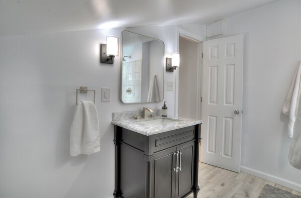 Un baño con lavamanos de mármol, muebles oscuros, un espejo grande y una puerta blanca.