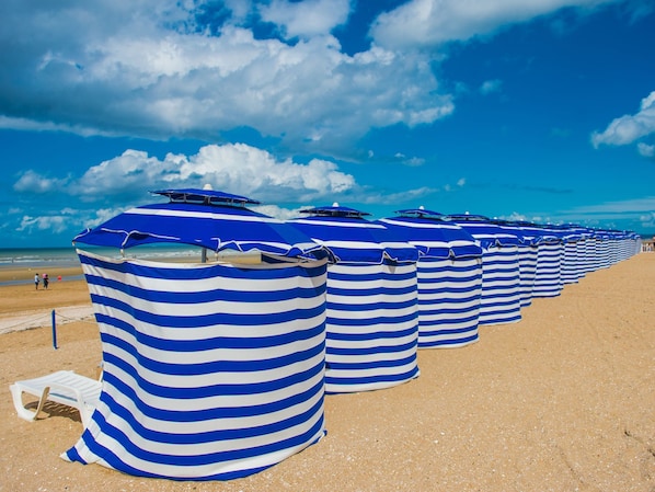Eine Reihe von gestreiften Strandsonnenschirmen an einem Sandstrand.