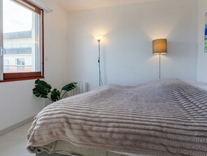 Une chambre à coucher avec un lit recouvert d’une couverture à motifs, une lampe de sol, une plante en pot et un radiateur.