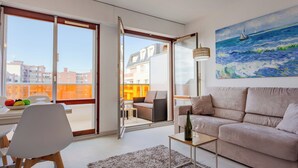 Een moderne woonkamer met een bank, een salontafel en een eethoek met stoelen en een schaal fruit.
