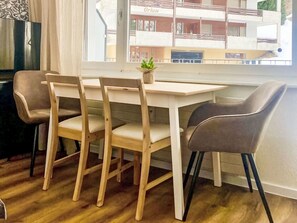 A dining area with a wooden table and four chairs, a small plant on the table, and a view of a building outside the window. - Flaminia by Interhome (Leukerbad)