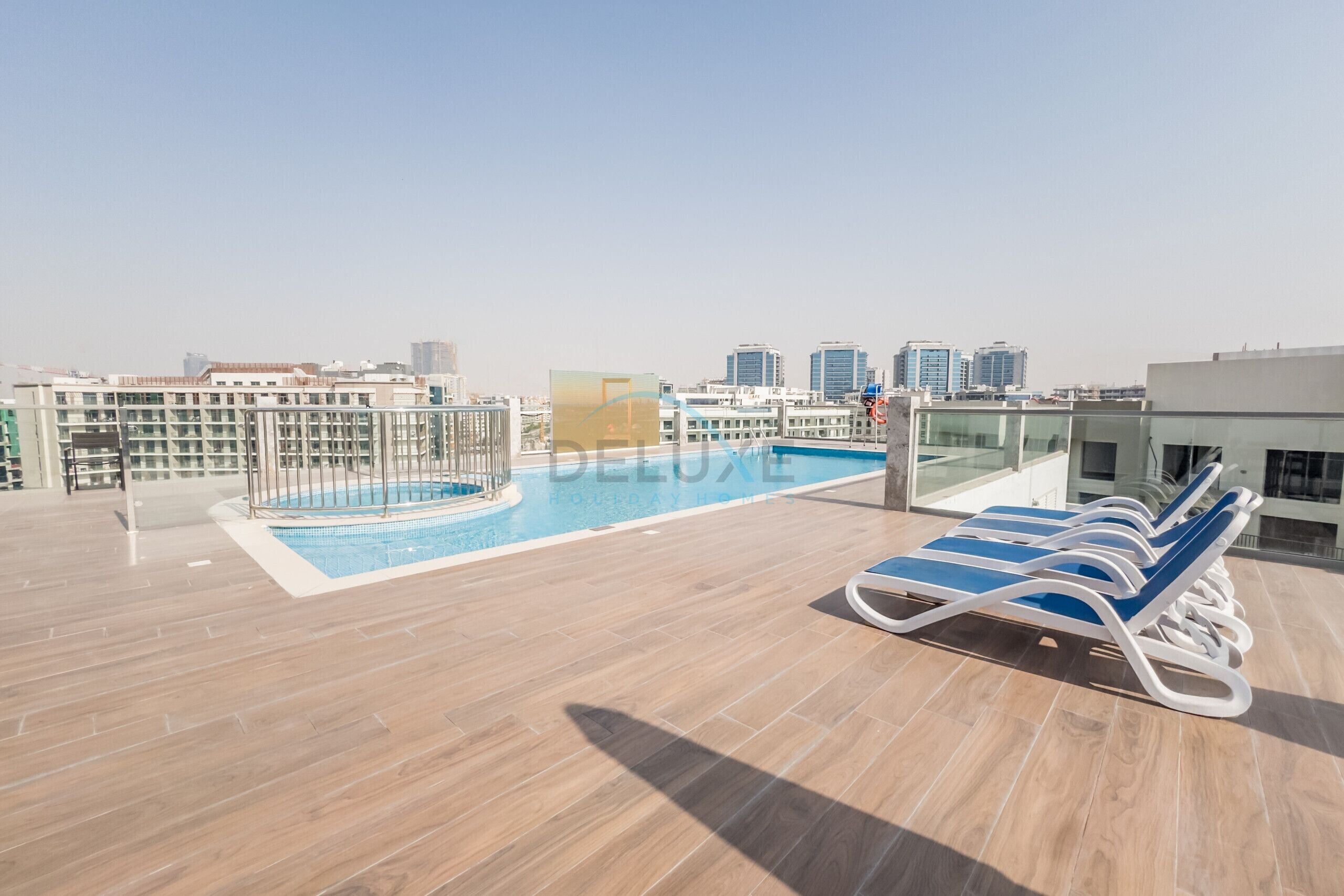 A rooftop pool area with lounge chairs, a pool, and a city skyline in the background.