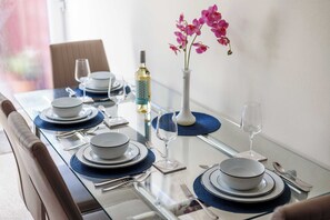 Una mesa de comedor dispuesta con platos, tazones, cubiertos y una botella de vino blanco.