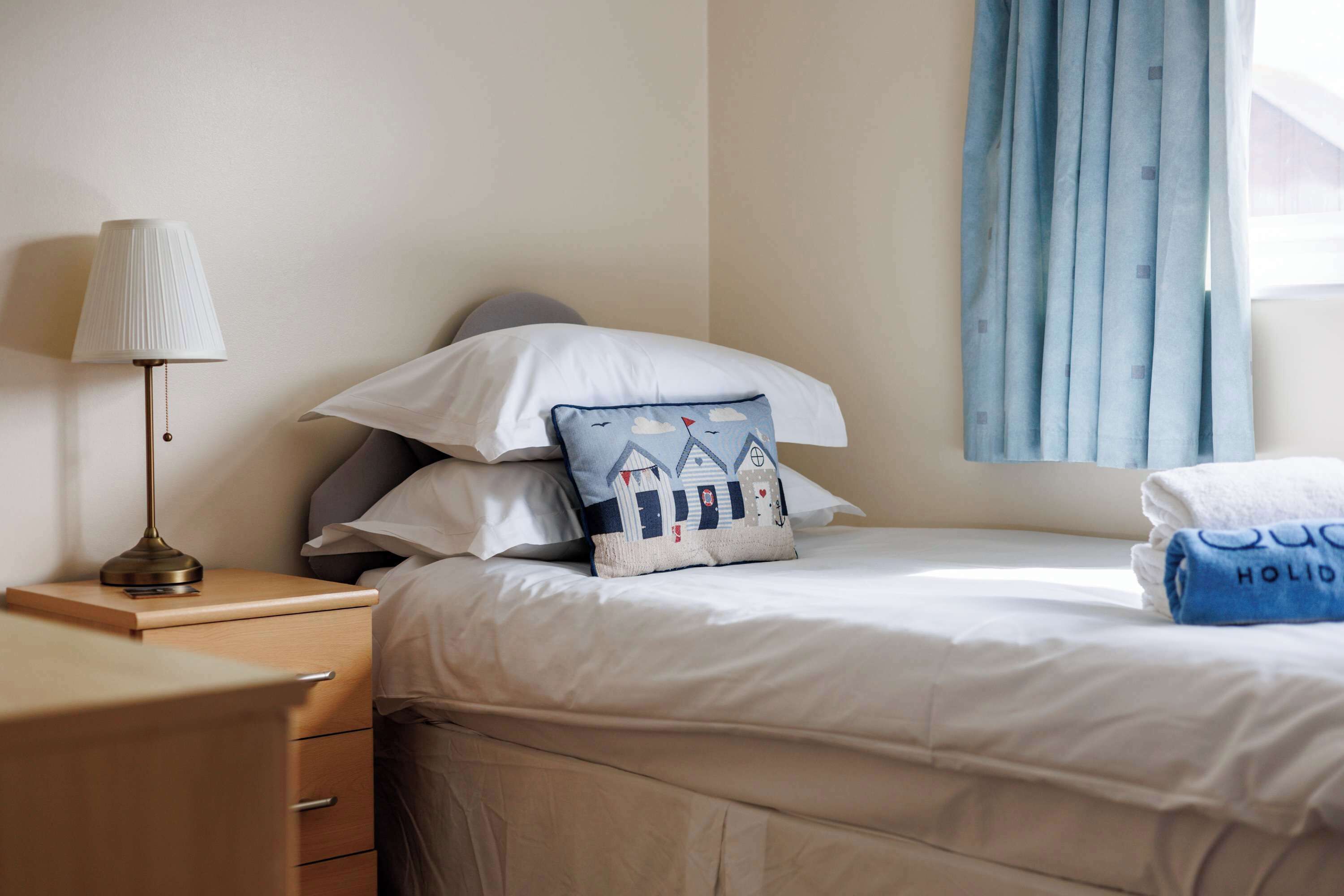 A neatly made bed with pillows, a bedside lamp, and a window with curtains.