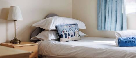 A neatly made bed with pillows, a bedside lamp, and a window with curtains.