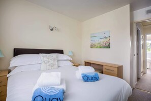 Habitación de hotel con cama, dos mesitas de noche, un aparador, un cuadro en la pared y una puerta que da a otra habitación.