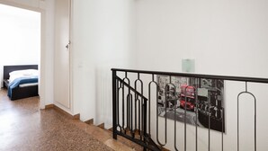 A staircase with a black metal railing, a bed with a white headboard, and a wall-mounted picture of a red double-decker bus. - Duplex with Terrace / Born, Arc de Triomf (08013 Barcelona)
