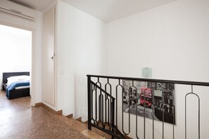 Eine Treppe mit schwarzem Metallgeländer, ein Bett mit weißem Kopfteil und ein an der Wand befestigtes Bild eines roten Doppeldeckerbusses.