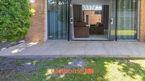 Uma casa moderna com porta de entrada de vidro, um pátio com mobiliário externo e um gramado bem cuidado.