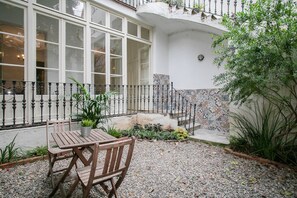 A courtyard with a wooden table and chairs, a tiled wall, and a balcony with a railing. - Authentic, Private Garden / Paseo de Gracia (08008 Barcelona)