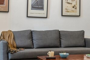 A grey sofa with a brown throw blanket, a coffee mug, and a bowl on a wooden table. - Authentic, Private Garden / Paseo de Gracia (08008 Barcelona)