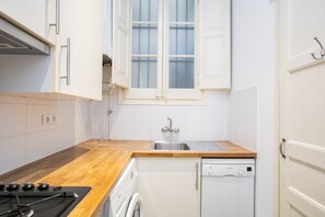 A compact kitchen with a wooden countertop, a built-in dishwasher, and a window with white shutters. - Authentic, Private Garden / Paseo de Gracia (08008 Barcelona)