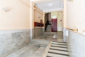 A marble-floored hallway with a staircase, a wall-mounted light fixture, and a door at the end. - Authentic, Private Garden / Paseo de Gracia (08008 Barcelona)
