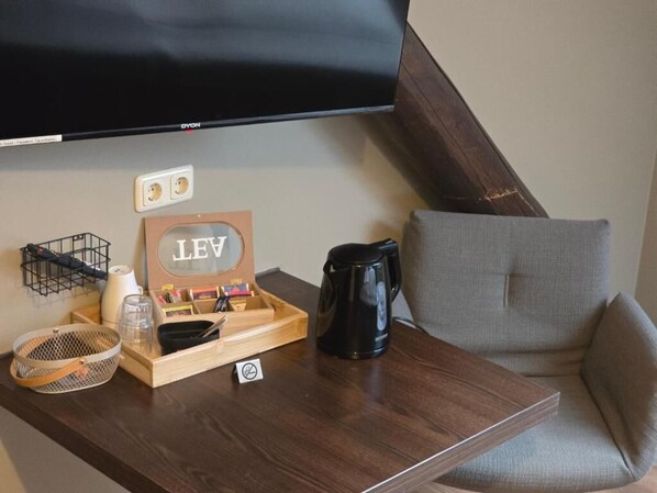 Una mesita de madera con una cafetera negra, una bandeja de madera con material de escritorio, una cesta de mimbre y un letrero con las letras "LEV".