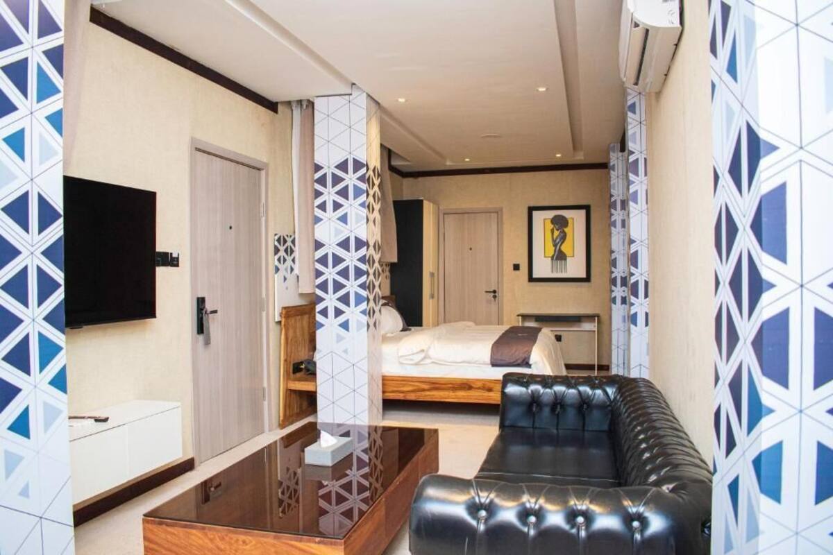 Una habitación de hotel moderna con sofá, cama, televisor y pared con diseño.