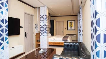 A modern hotel room with a sofa, a bed, a TV, and a patterned wall.