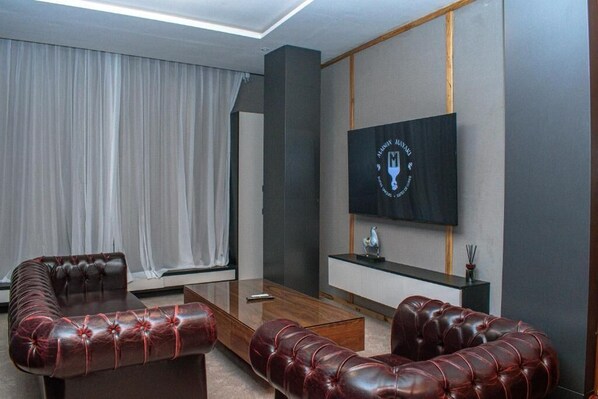 A modern living room with a large flat-screen TV mounted on the wall, leather sofas, and a glass coffee table. - MAISON MAYAKI (Lomé)