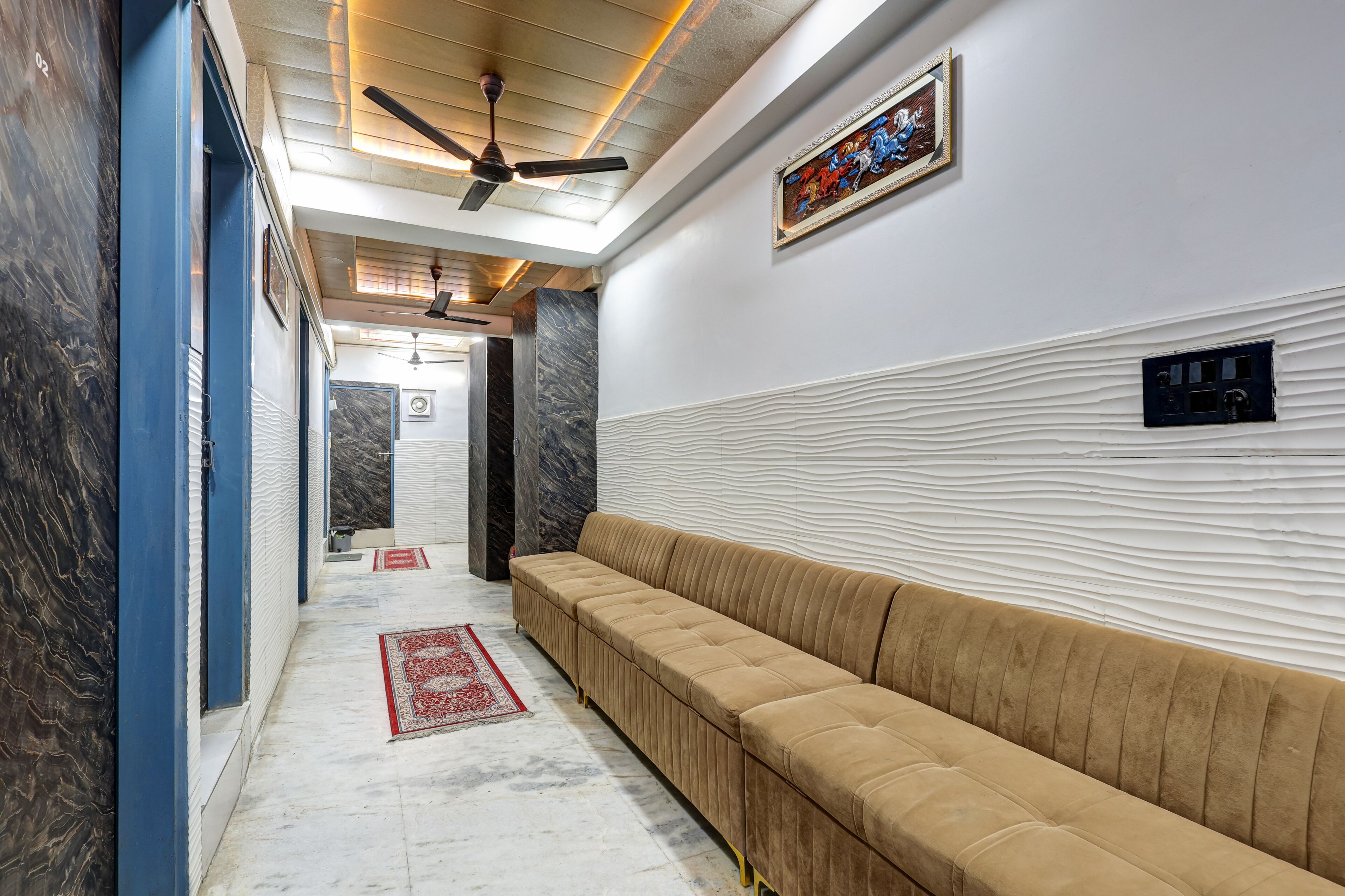 A hallway with a beige sofa, ceiling fans, marble flooring, and a red rug.