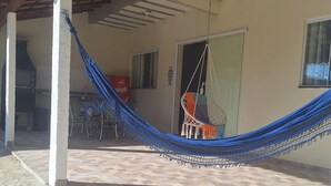 A covered patio with a hammock, tiled flooring, and a door leading to a kitchen area. - Complete House in Pontal do Peró: Comfort and nature next to Búzios (Cabo Frio)