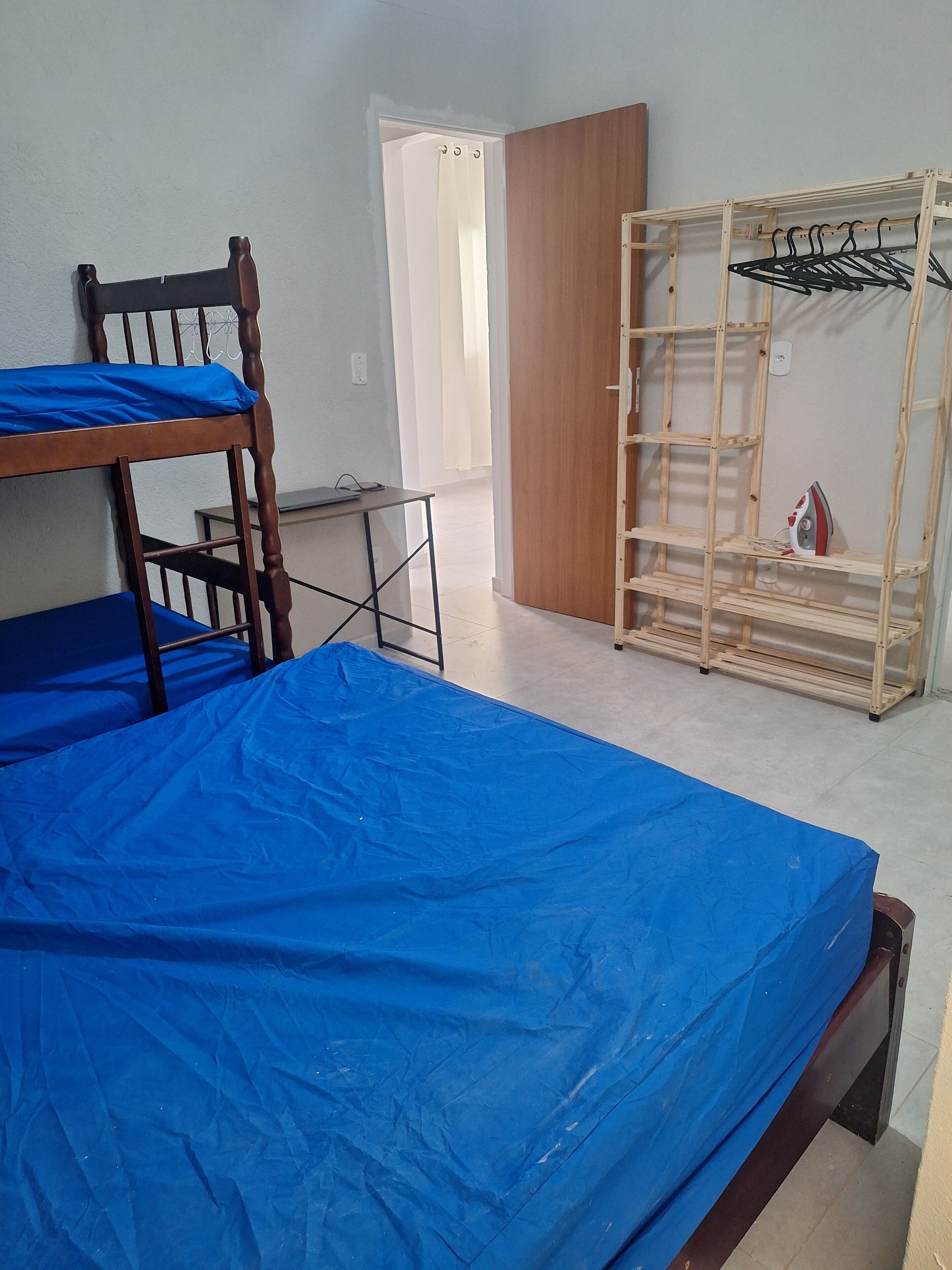 A room with bunk beds, a wooden wardrobe, and a metal drying rack.