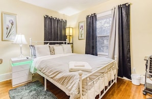 A neatly arranged bedroom with a bed, bedside table, lamp, and a window with curtains. - Fabulous 5-bedroom house with AC Perfect for Family and Extended Stays (Rochester)