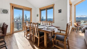 A dining area with wooden chairs and a table set for four, large windows with a view of snow-capped mountains, and a wooden ceiling. - Alma Mountain Escape - Views , Deck , Theater (Fairplay)