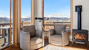 A cozy room with two patterned armchairs, a telescope, and a wood-burning stove, overlooking a snowy mountain landscape. - Alma Mountain Escape - Views , Deck , Theater (Fairplay)