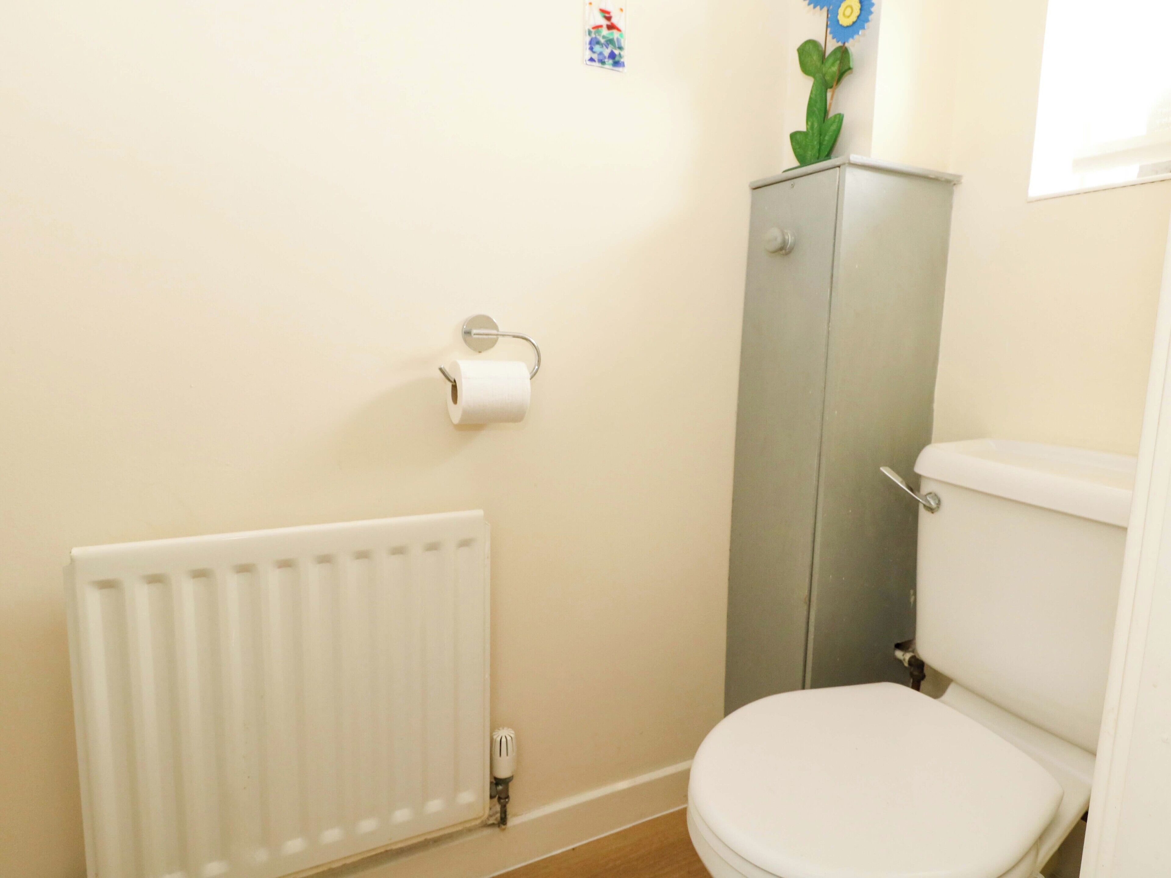 A bathroom with a toilet, radiator, and a cabinet with a flower decoration.