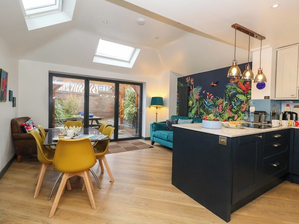 A modern kitchen with a central island, a dining area with yellow chairs, and a living space with a teal sofa.