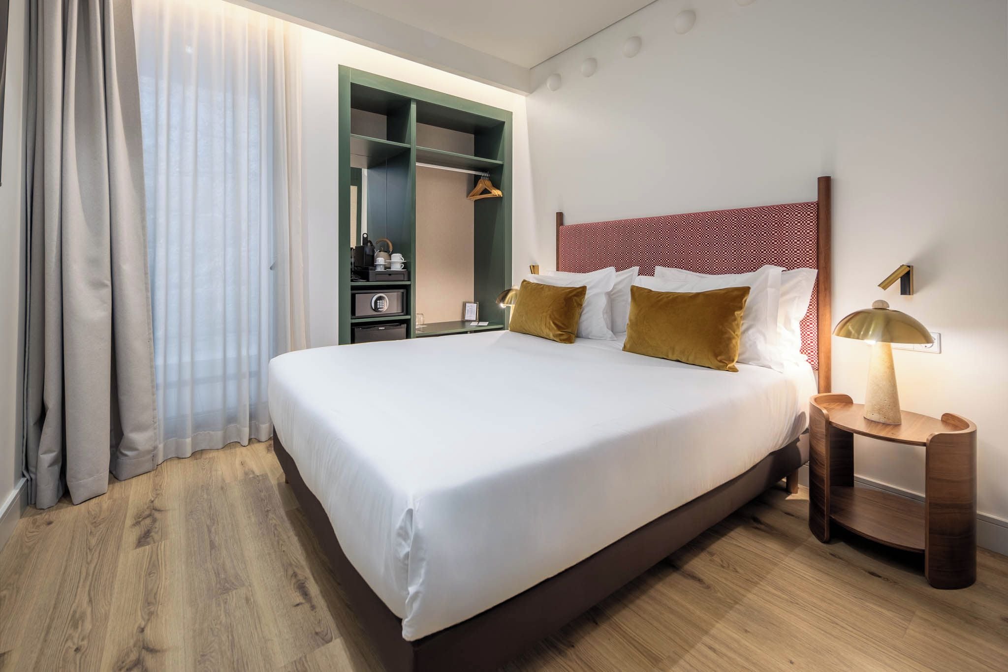 Una habitación de hotel con una cama grande, una mesita de noche con lámpara, un armario y un espejo.