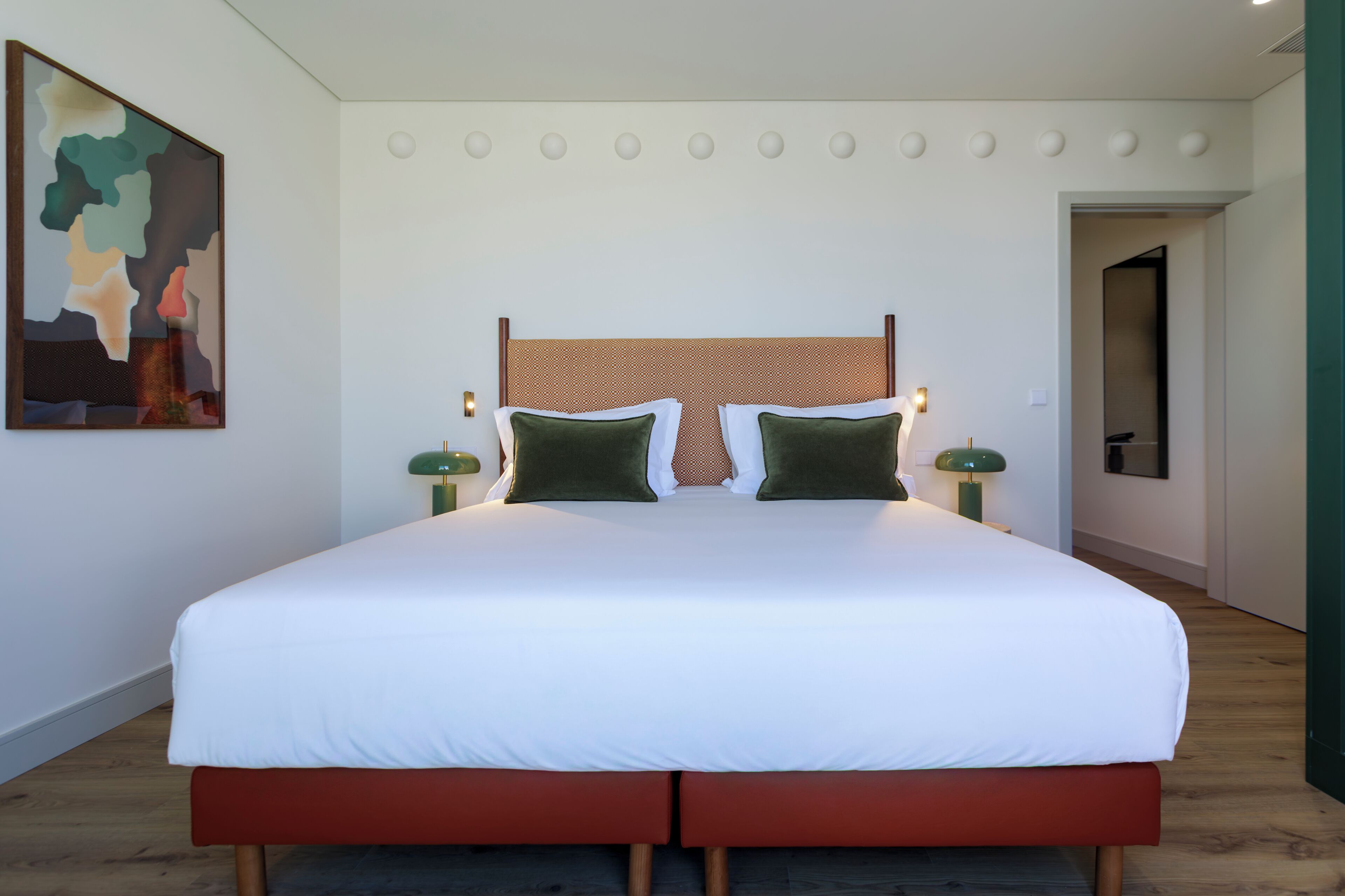 A neatly made bed with a white mattress and green pillows, a wooden headboard, and two bedside lamps.