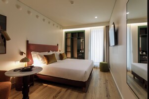 Habitación de hotel con cama, mesita de noche, lámpara, espejo y vistas al exterior.