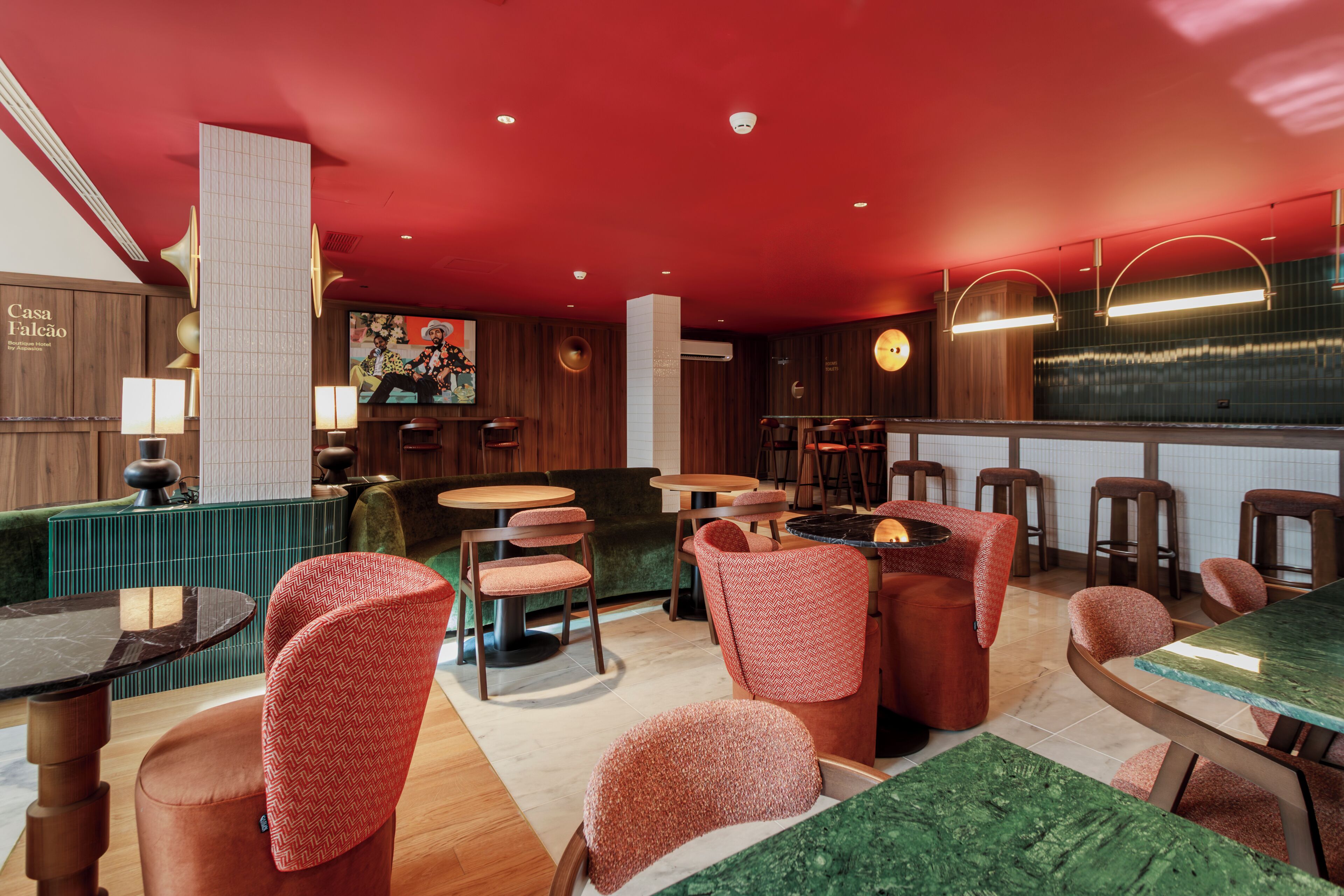 L’intérieur d’un restaurant présente des murs en bois, un plafond rouge et plusieurs espaces aménagés avec des tables rondes et des chaises rembourrées.