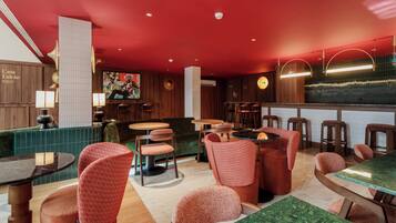 L’intérieur d’un restaurant présente des murs en bois, un plafond rouge et plusieurs espaces aménagés avec des tables rondes et des chaises rembourrées.