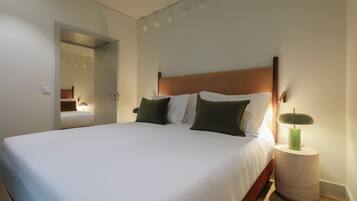 A neatly made bed with white linens and green pillows, a round bedside table with a lamp, and a wooden headboard.