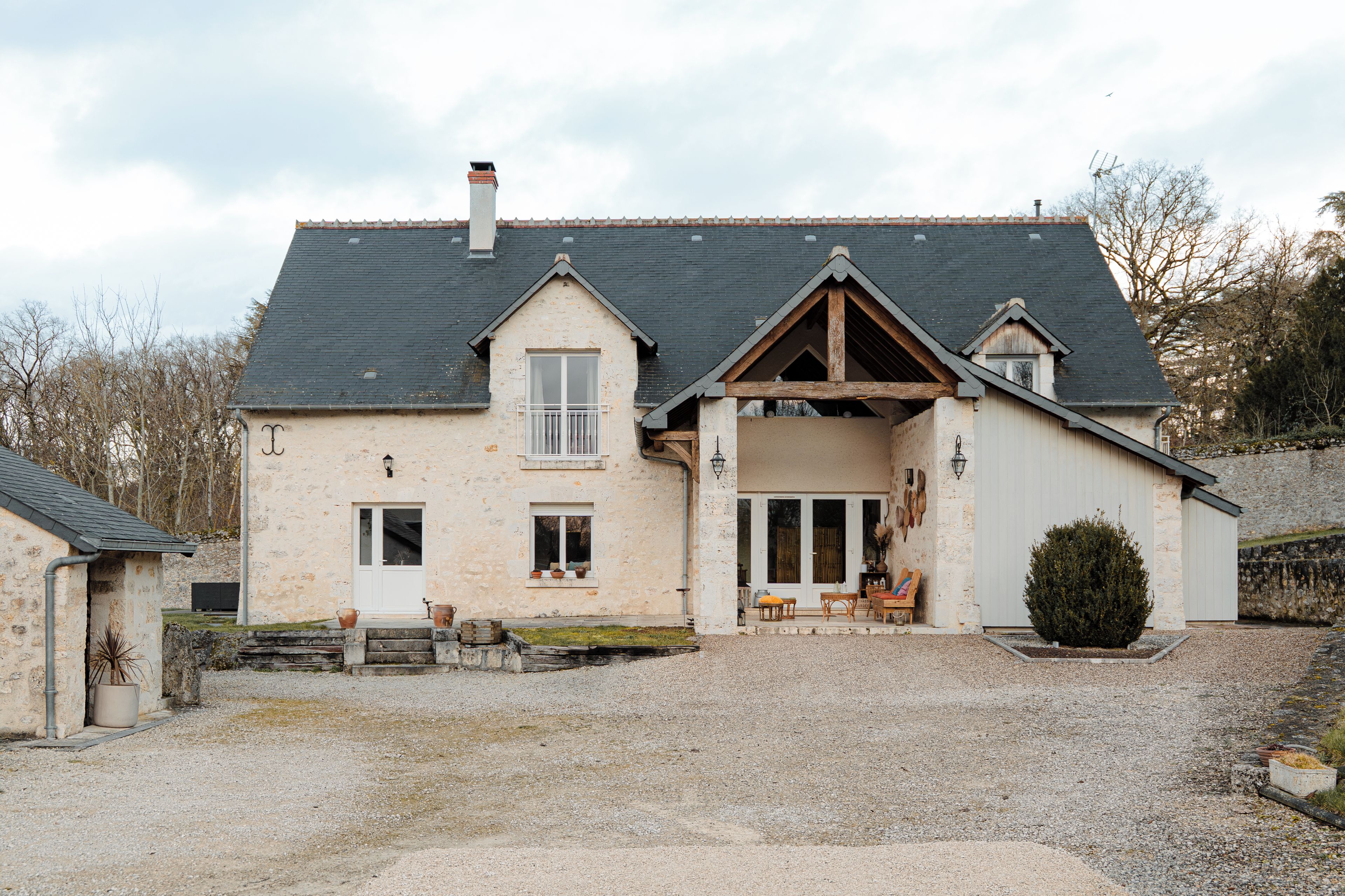 Une maison à deux étages avec un toit en pente, un porche à l’avant doté de sièges et une allée gravillonnée.