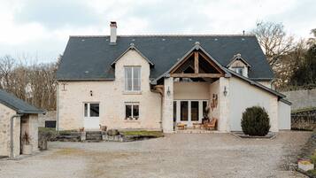 Une maison à deux étages avec un toit en pente, un porche à l’avant doté de sièges et une allée gravillonnée.