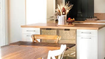 A kitchen with a wooden table, white chairs, a white cabinet, and a black stove.